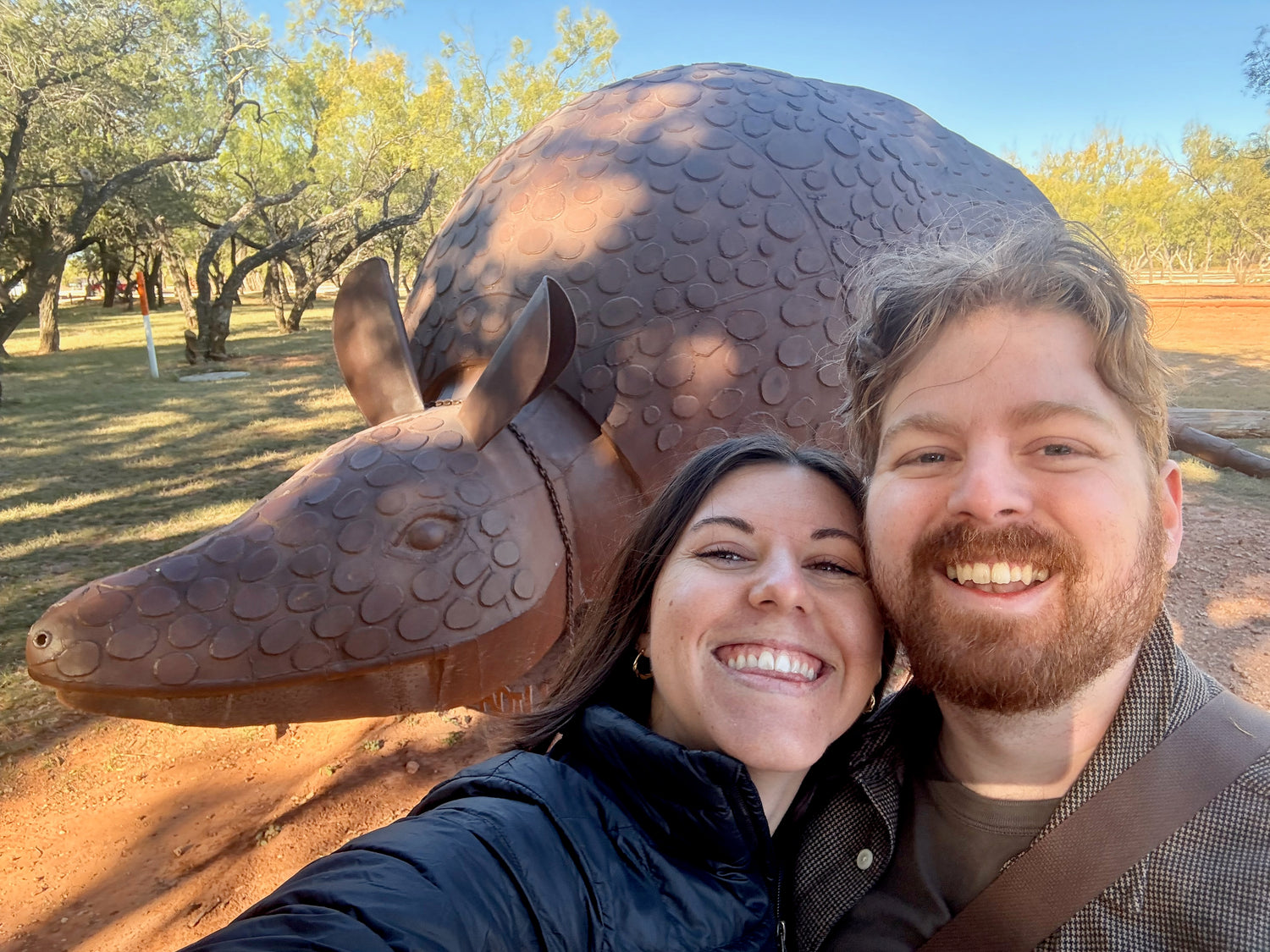 Kelly and Thomas posing with a large armadillo sculpture outdoors.